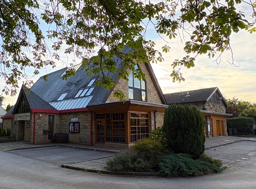 Oakwood Church on Springwood Road from the car park — a stone building with a steep slate roof and glazed wooden entrance, framed by chestnut branches overhead